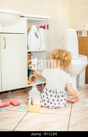 Unattended girl child play quietly at bathroom with dangerous household chemicals. Safety hazard at home concept. Keep away from children`s reach. Stock Photo
